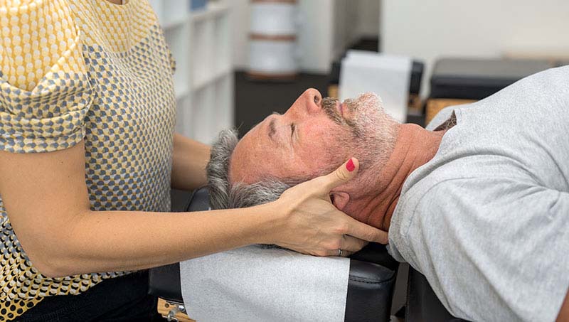 Man receiving a neck adjustment from a Woman in need of an adjustment for whiplash pain by a Ponderay Chiropractor at By Design Chiropractic